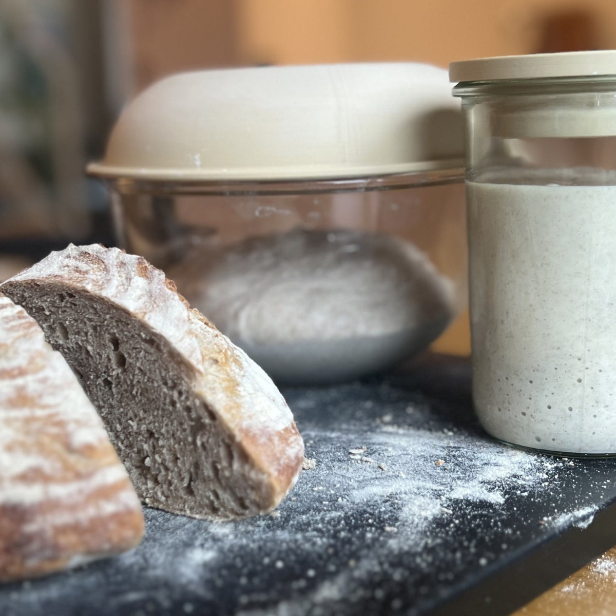 Sliced sourdough loaf next to the Peak Dough starter jar and proofing bowl